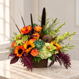 Bright mixed floral arrangement in a wooden container with sunflowers and orchids