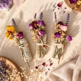 Three small dried flower bundles tied with twine on a light fabric surface.