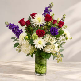 Bouquet of red roses, white dahlias, and purple flowers in a glass vase