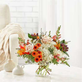 Mixed bouquet of pale roses, white blooms, and orange flowers in a clear vase