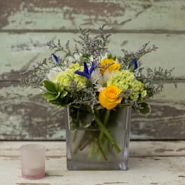 Yellow roses and white flowers in a square glass vase