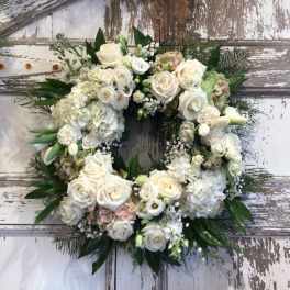 White floral wreath with roses and hydrangeas on a rustic door