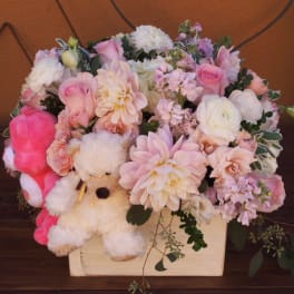 Pink and white flower arrangement in a wooden box with a teddy bear
