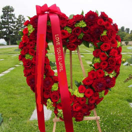 Heart-shaped red rose wreath on an easel with a red ribbon