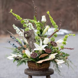 White lilies and roses in a wicker basket with branches and seed pods