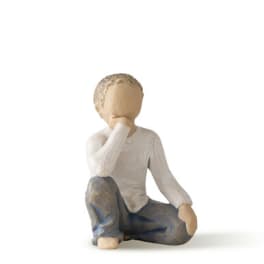 Small carved figurine of a seated child in a white shirt and blue pants