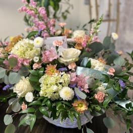 Mixed pastel flower arrangement in a white basket with roses and chrysanthemums