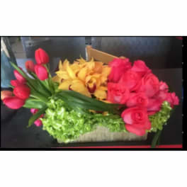 Colorful floral arrangement with tulips, roses, and orchids in a low container