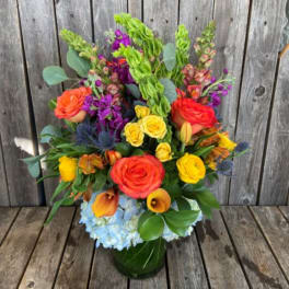 Colorful mixed bouquet with roses, calla lilies, and blue hydrangea in a green vase