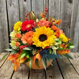Mixed autumn bouquet with sunflowers, gerbera daisies, and orange roses in a pumpkin vase