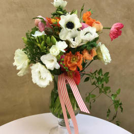 Mixed bouquet of white, orange, and pink flowers in a glass vase with a striped ribbon