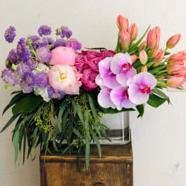 Colorful bouquet with purple blooms, pink roses, orchids, and tulips in a glass vase