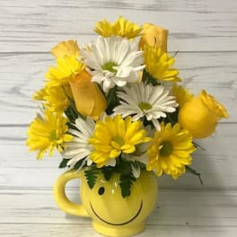 Yellow and white daisy bouquet in a smiley-face mug