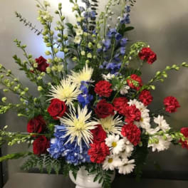 Tall mixed flower arrangement in a white vase with red, white, and blue blooms