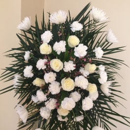 White floral standing spray with roses and carnations on dark palm fronds