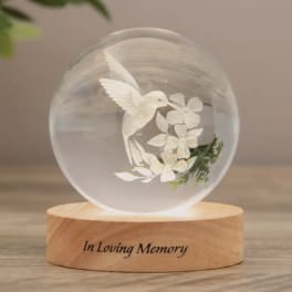 Glass orb memorial light with a white hummingbird and flowers on a wooden base