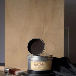Tin of black wax with a brush beside it on a tabletop