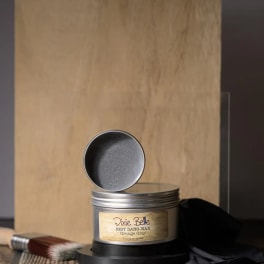 Tin can of gray wax with an open lid and a brush beside it