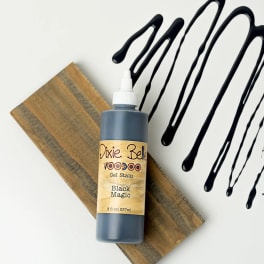 Bottle of black gel stain on a wood board with black drips nearby