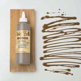 Bottle of wood stain on a wooden board beside brown paint swatches