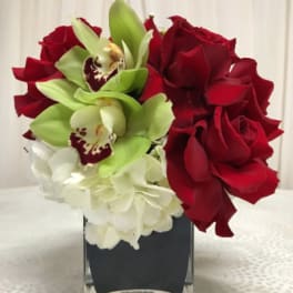 Red roses, green orchids, and white hydrangeas in a square glass vase