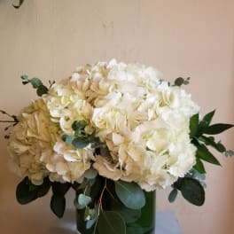 White hydrangea bouquet in a green glass vase with eucalyptus
