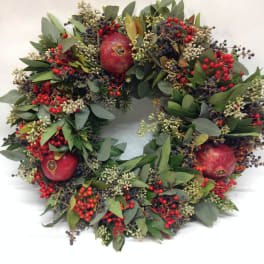Round wreath of greenery, berries, and pomegranates on a white background