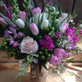 Bouquet of pink and white tulips, roses, and purple flowers in a burlap-wrapped vase