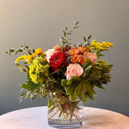 Mixed bouquet of pink, red, and yellow flowers in a clear glass vase