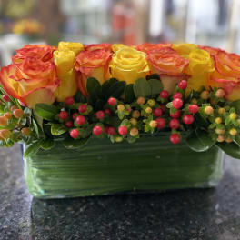 Yellow and orange roses in a rectangular glass vase with berry accents