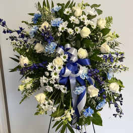 Tall blue and white standing spray with roses, carnations, daisies, and a blue and white bow on an easel.