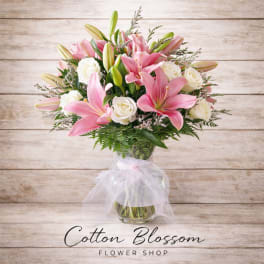 Pink lilies and white roses in a glass vase with a sheer ribbon