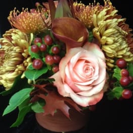 Compact autumn-toned arrangement with a peach rose, bronze blooms, and berries in a brown vase