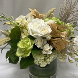 Low arrangement of white and green flowers with dried leaves in a clear glass vase