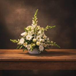 White floral arrangement in a low white bowl on a wooden table