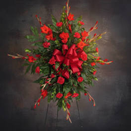 Red floral standing spray with a large ribbon on a black easel