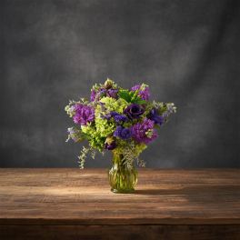Purple and green flower arrangement in a glass vase