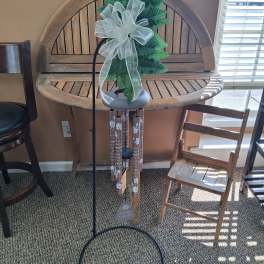 Memorial wind chime with faux greenery and a white bow on a metal stand