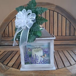White memorial lantern with a candle, ribbon bow, and greenery on top