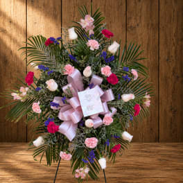 Standing floral spray with pink, white, and purple flowers on a ribboned easel