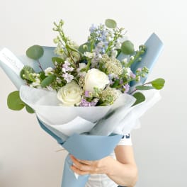 Bouquet of white roses and pastel flowers wrapped in blue and white paper