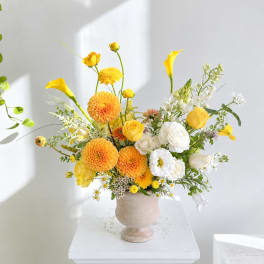 Yellow and white floral arrangement in a beige pedestal vase