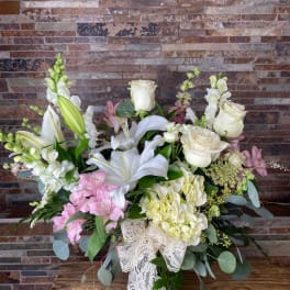 White lilies and roses with pink blooms in a glass vase with lace ribbon