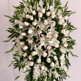Large white funeral spray with roses and lilies on a stand