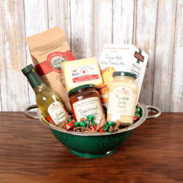 Gourmet food gift set arranged in a green metal colander on a wooden surface.