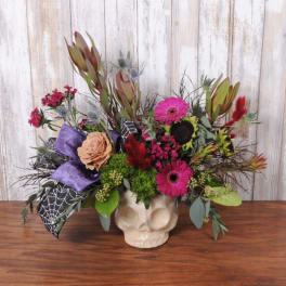 Colorful floral arrangement in a skull-shaped vase with purple ribbon