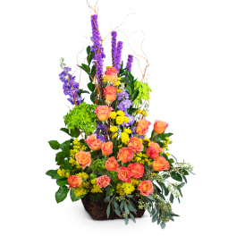 Tall arrangement of orange roses, purple spikes, and yellow flowers in a basket