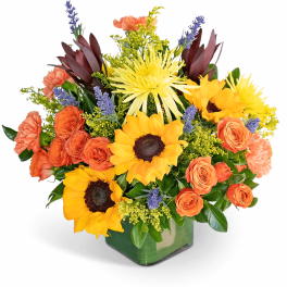 Bright mixed bouquet with sunflowers, orange roses, and purple accents in a square vase