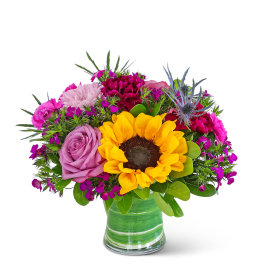Bright mixed bouquet with a sunflower and pink roses in a green glass vase