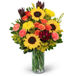 Sunflowers, orange roses, and pink carnations in a glass vase